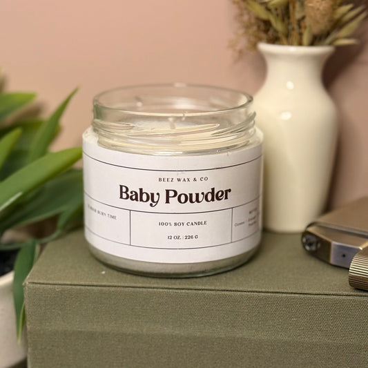 Jar of 'Baby Powder' candle on a green surface with decorative items in the background