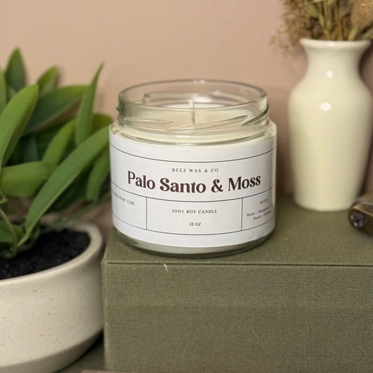 Candle labeled 'Palo Santo & Moss' on a green surface with plants and a vase in the background.