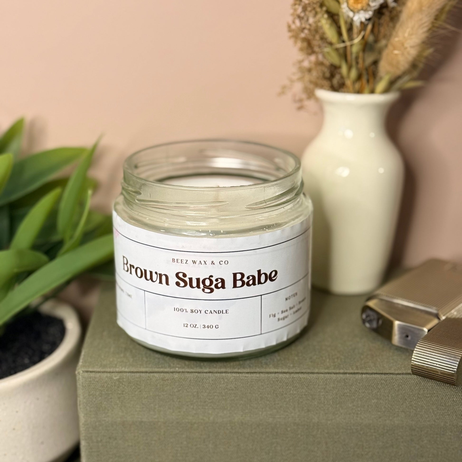 Jar of 'Brown Suga Babe' candle on a green surface with decorative items in the background.